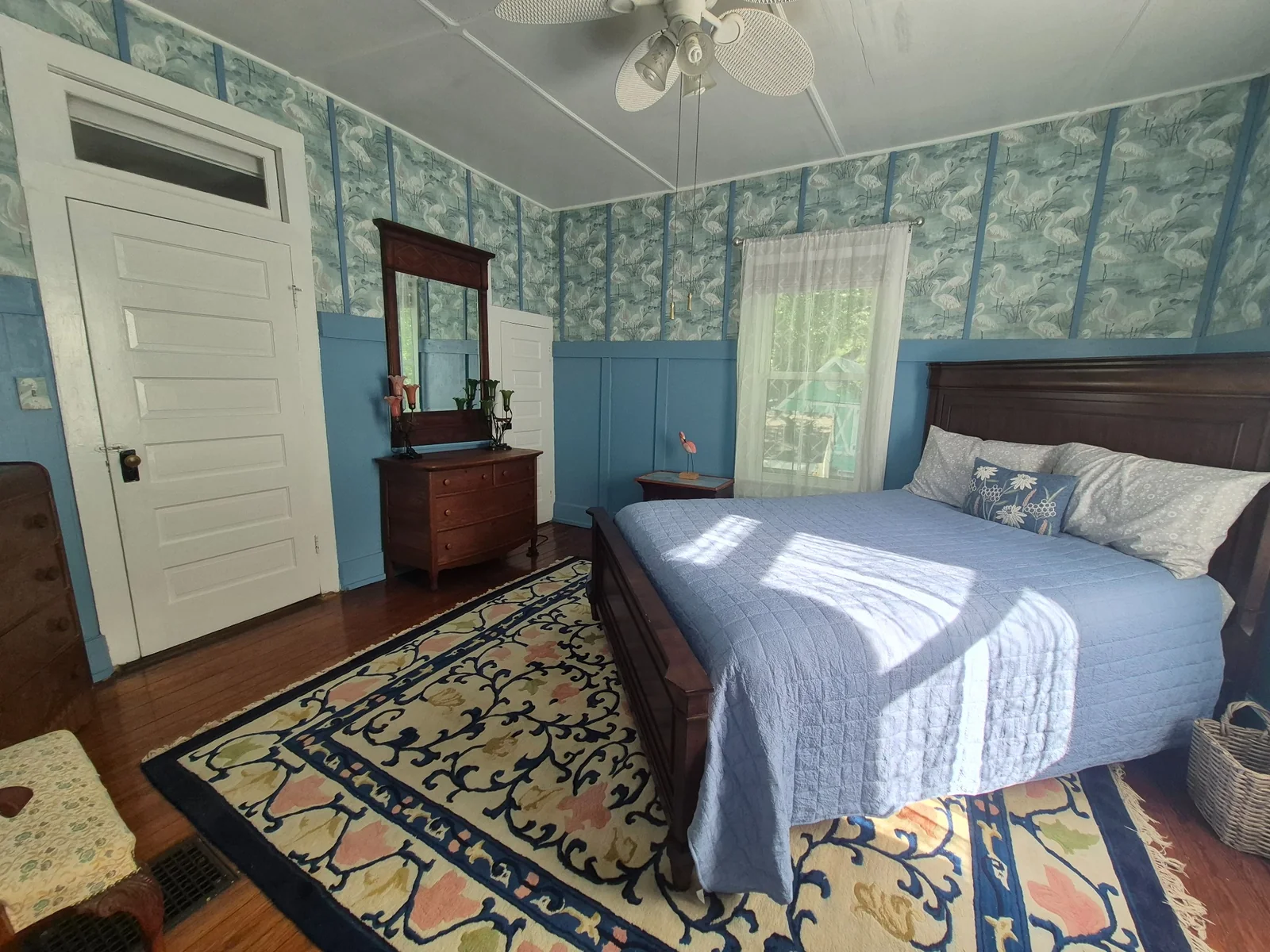 Blue bedroom with a dark wood bed and heron-pattern wallpaper